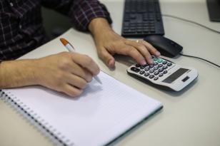 Pessoa com calculadora e caderno na mesa